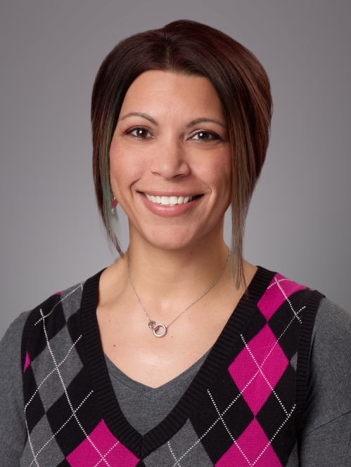 Headshot of female with short hair wearing a pink and black argyle sweater over a long grey sweater.