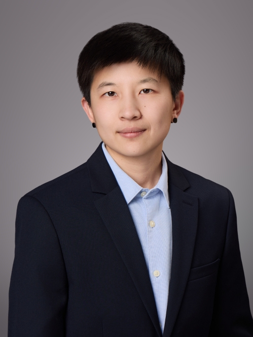 Headshot of female with short black hair and black post earrrings, wearing a light blue button down shirt and black jacket.