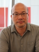 head shot of Asian man with eyeglasses and wearing a grey button down shirt