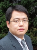 head shot of asian man with short black hair and eyeglasses wearing a grey suit, grey tie, and a white shirta