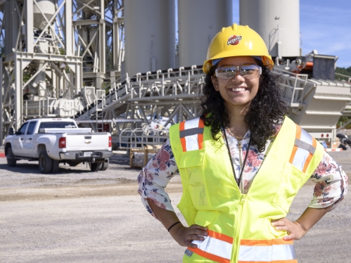 Young woman with long brown curly hair wearing a hard hat and yellow safety vest conducting research with Bechtel