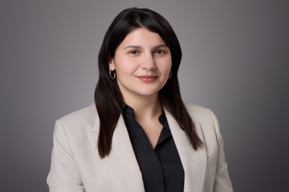 Headshot of woman with long brown hair wearing a black blouse and a light brown jacket.
